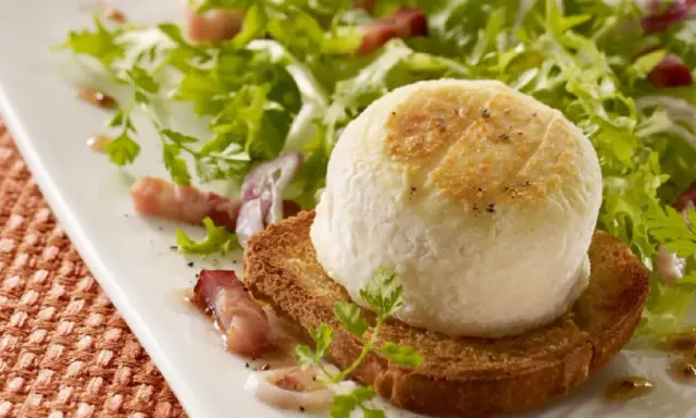 Une délicieuse salade de chèvre chaud sur toast, garnie de lardons et de persil frais, sur une assiette blanche.