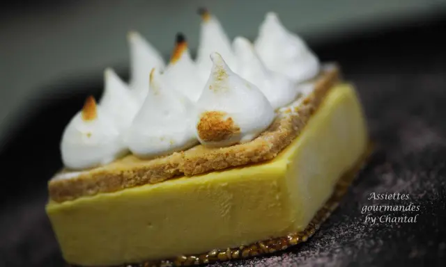 Une tranche de tarte au citron meringuée, avec sa crème jaune pâle, sa fine couche de biscuit et ses pointes de meringue légèrement caramélisées.
