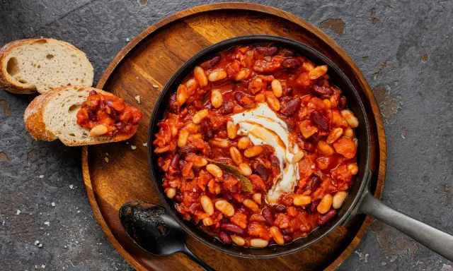 Délicieuse recette baked beans dans une poêle, garnie de crème, servie avec du pain grillé. Un plat réconfortant et savoureux.