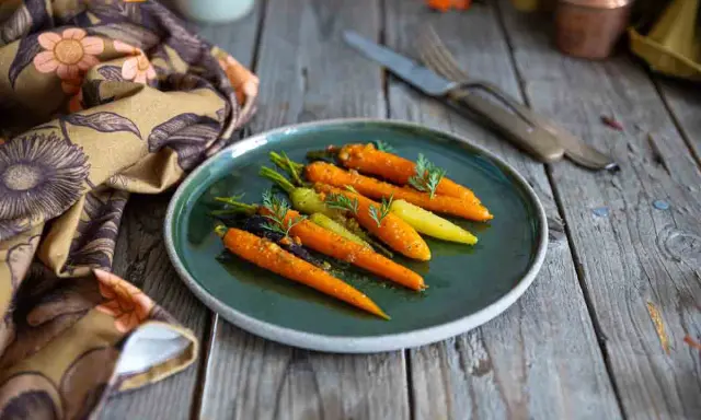 Carottes glacées au miel, colorées et appétissantes, garnissent une assiette sur une table en bois rustique. Une serviette à motifs floraux complète la scène.