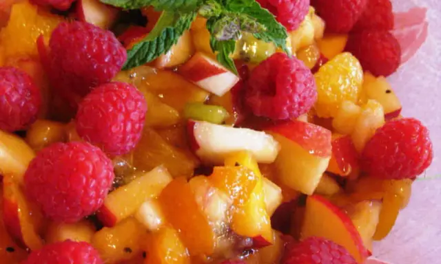 Une délicieuse salade de fruits d'été, pleine de framboises, pêches et abricots juteux, garnie de menthe fraîche.
