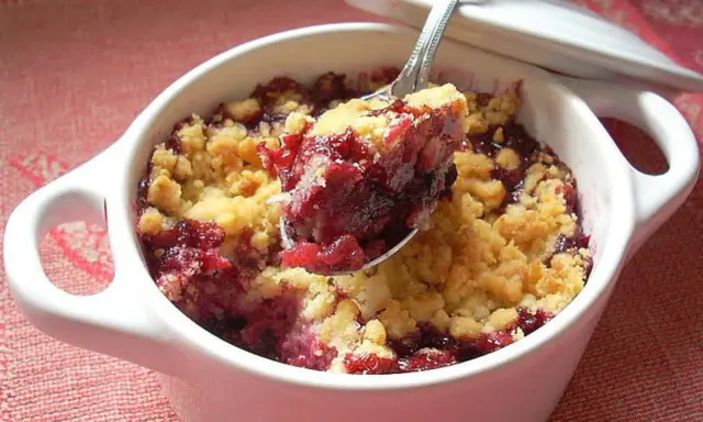 Cuillère de crumble fruits rouges, un délice croustillant et fruité dans un ramequin blanc.