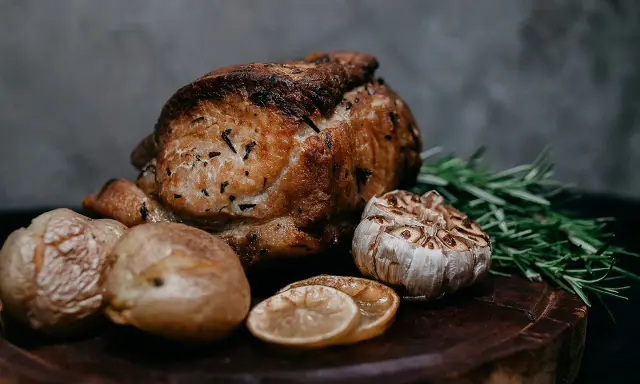 Un délicieux roti de veau au four, accompagné de pommes de terre rôties, d'ail confit, de rondelles de citron et de romarin frais sur une planche en bois.