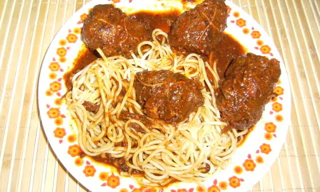 Un plat de spaghetti avec des ragoûts de bœuf en sauce, ressemblant à des alouettes sans tête, sur une assiette décorée de fleurs.