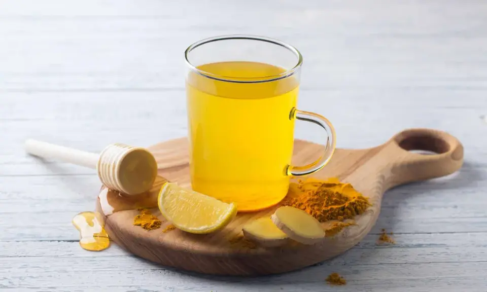 Une tasse de boisson gingembre citron curcuma, avec des tranches de citron, du gingembre frais et du curcuma en poudre.