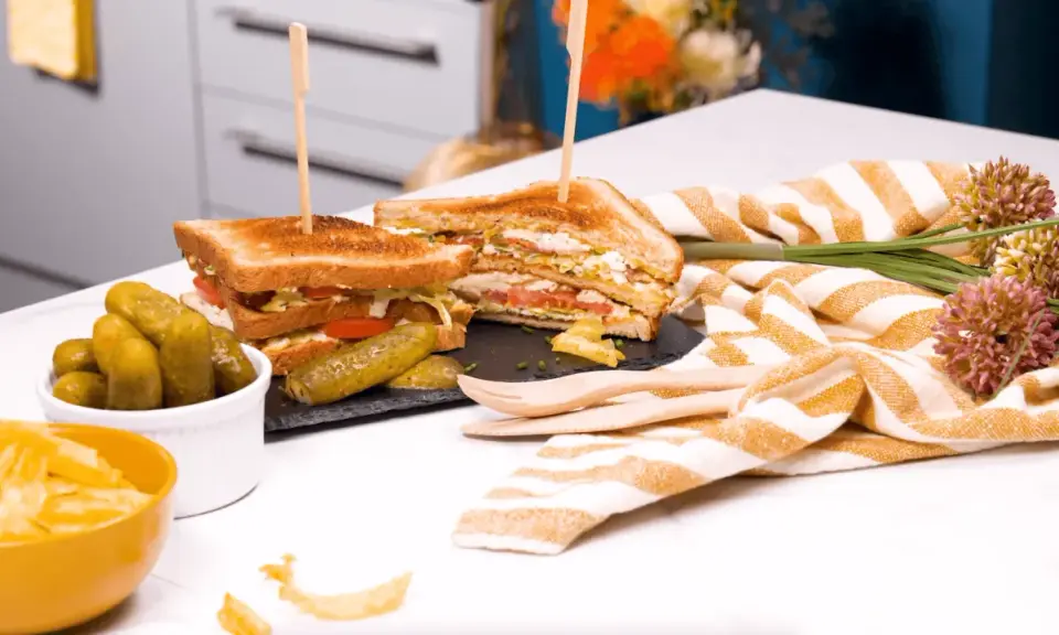 Un délicieux club sandwich, garni de tomates et de laitue, servi avec des cornichons et des chips.