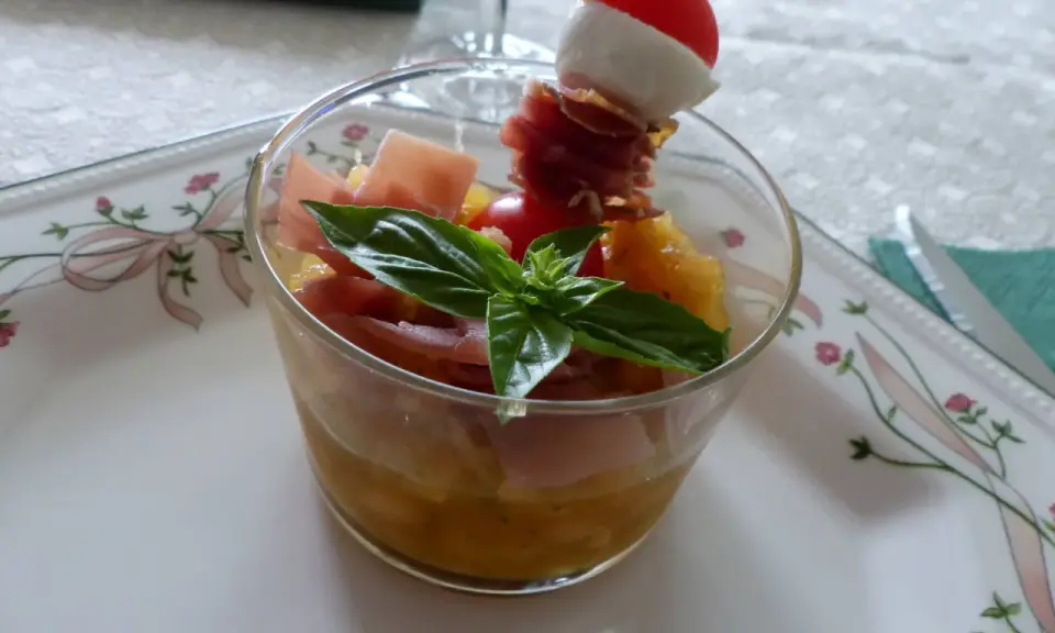 Verrine melon jambon cru : dés de melon, jambon cru, mozzarella et tomate cerise sur un pic. Une feuille de basilic décore ce délice.