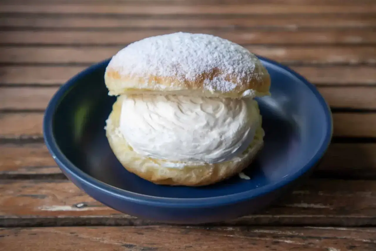 Un déliceux chou à la crème, saupoudré de sucre glace, repose dans une assiette bleue sur une table en bois.