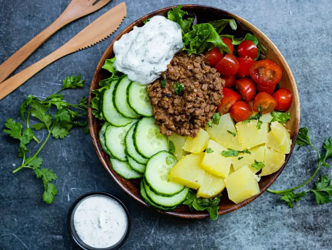 Salade repas colorée avec viande hachée, pommes de terre, tomates cerises, concombre, laitue et sauce blanche.