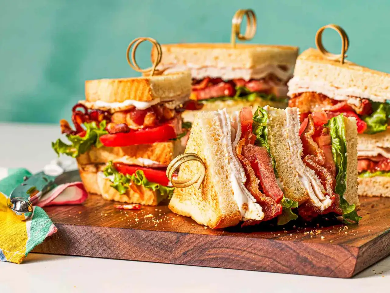 Plusieurs club sandwichs appétissants, garnis de bacon croustillant, de tomates juteuses et de laitue fraîche, sur une planche en bois.