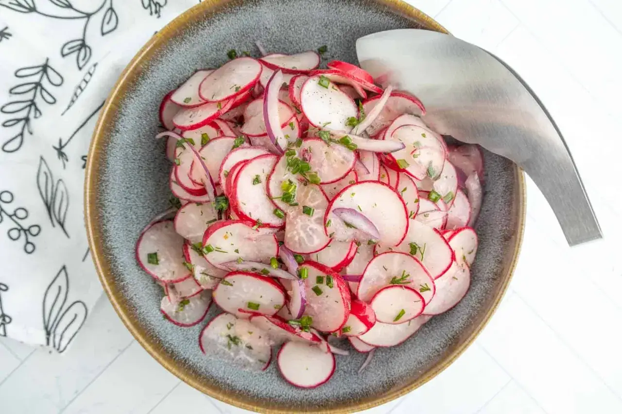 Une assiette de salade de radis rose croquants, parsemée d'herbes fraîches et d'oignons rouges. Parfait pour un repas léger.