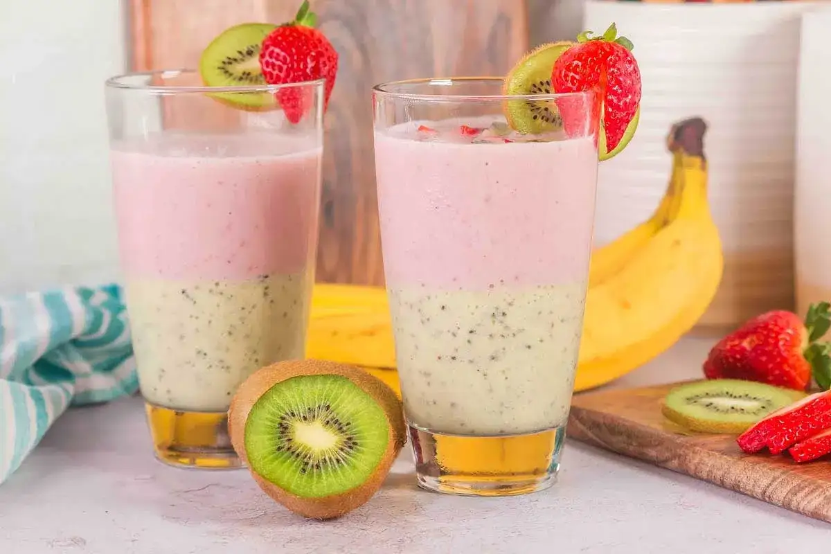 Deux verres de smoothie banane kiwi, décorés de fraises et de kiwi. Un délice fruité et rafraîchissant.