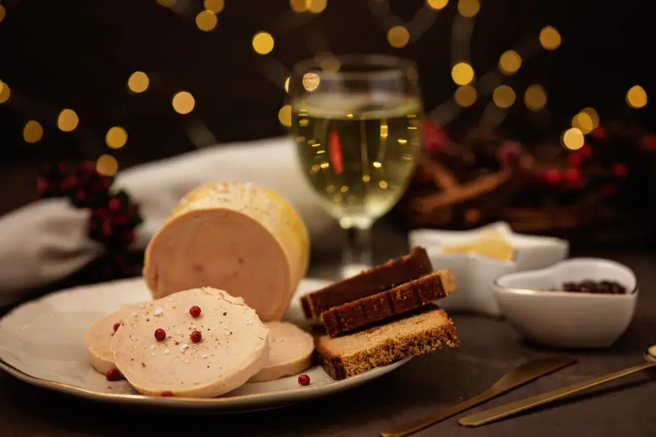 Tranche de vin foie gras sur une assiette, avec du pain d'épices et un verre de vin blanc. Ambiance festive avec des lumières douces.