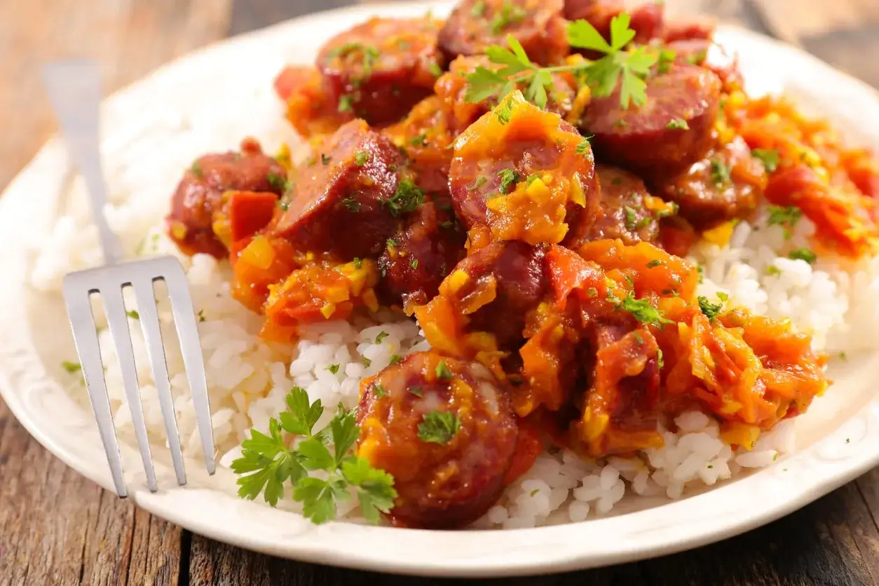 Rougail saucisse savoureux sur un lit de riz blanc, garni de persil frais. Quel vin avec rougail saucisse ? Un vin fruité et léger serait parfait.