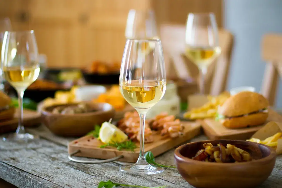 Verre de vin blanc sec ou moelleux, accompagné de crevettes, frites et mini-burgers sur une table rustique.