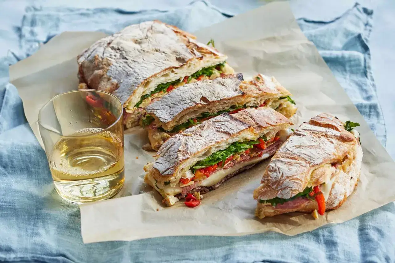 Un d&eacute;licieux sandwich italien garni de charcuterie, de fromage et de l&eacute;gumes frais, pr&ecirc;t &agrave; &ecirc;tre d&eacute;gust&eacute; avec un verre de vin blanc.