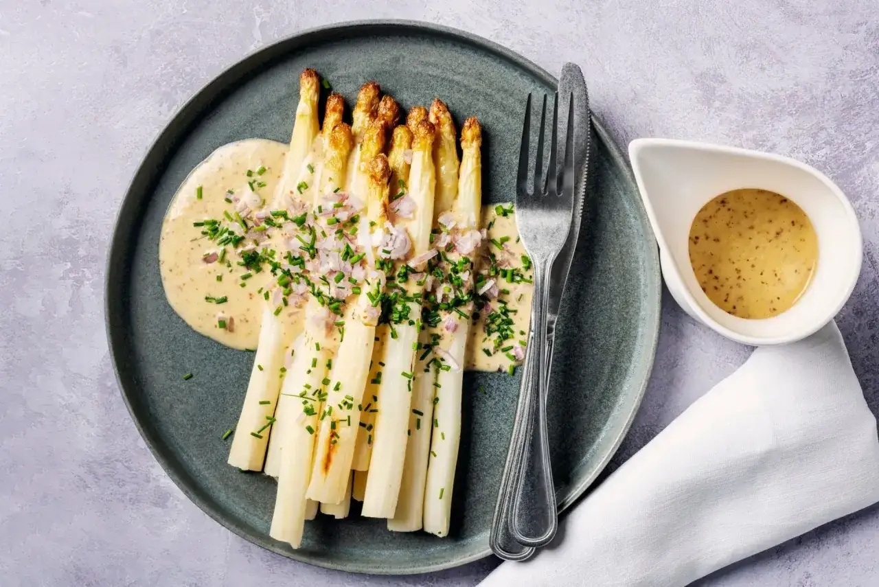 Asperges blanches en entr&eacute;e froide, napp&eacute;es d'une sauce cr&eacute;meuse et garnies de ciboulette et d'&eacute;chalotes. Un d&eacute;lice printanier.
