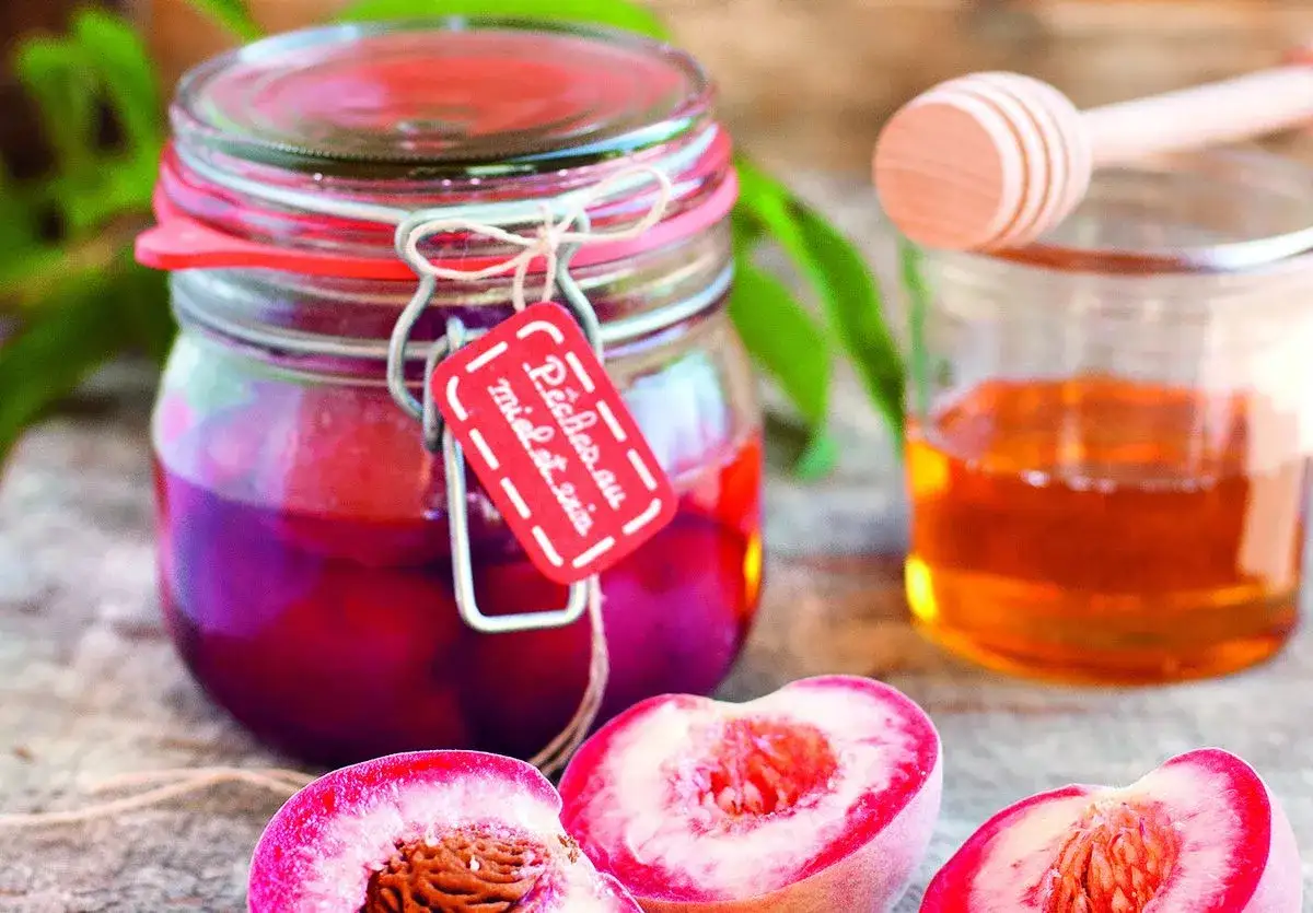 Un bocal de confiture pêches de vignes, avec des pêches coupées et un pot de miel à côté.