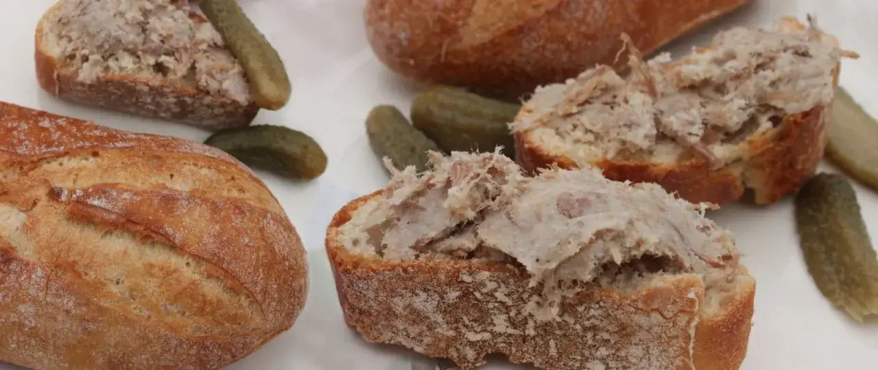 Tranches de pain garnies de rillettes de porc, accompagnées de cornichons croquants. Un délice rustique.