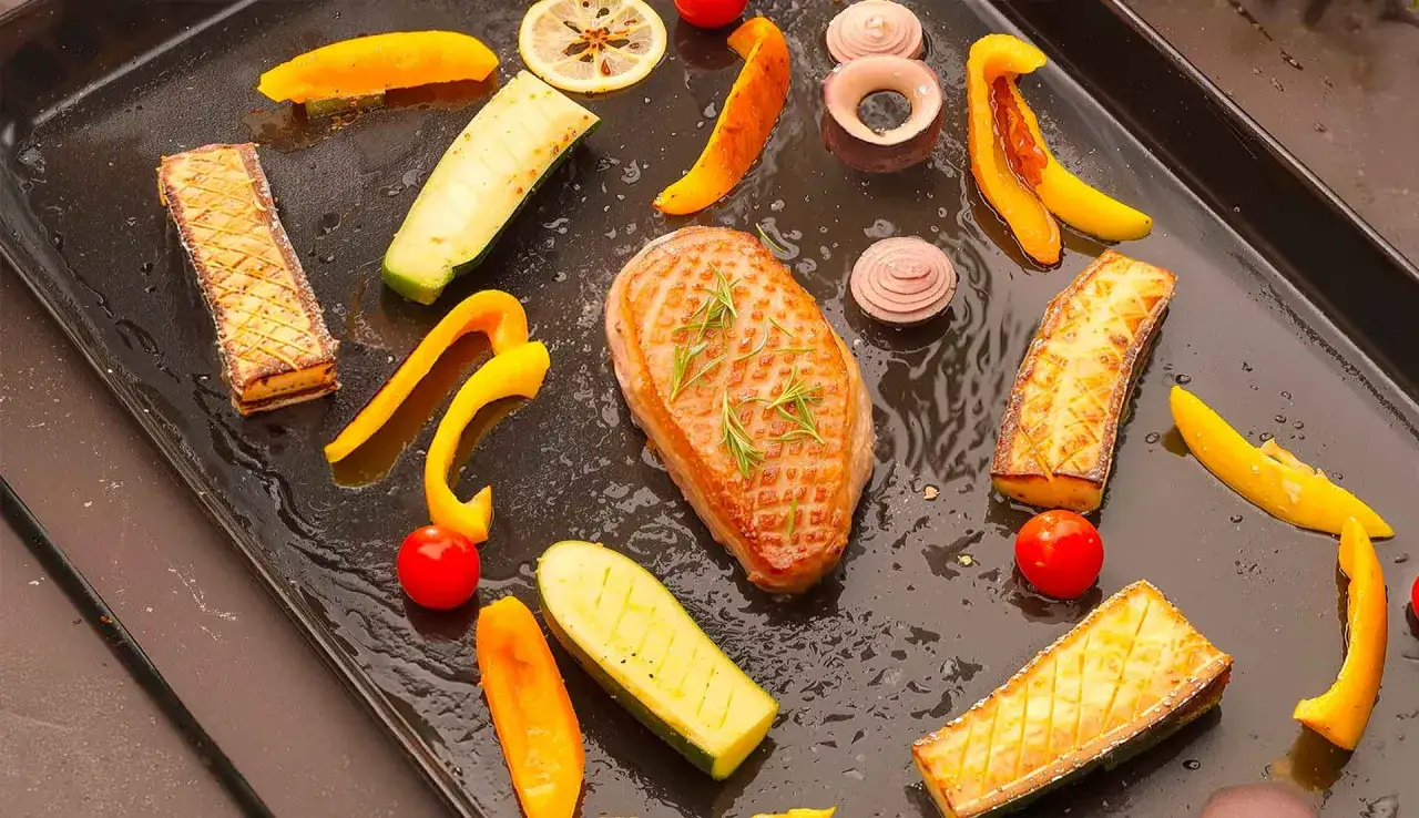 Magret de canard en cuisson sur plancha, entouré de légumes colorés et de tranches de citron.