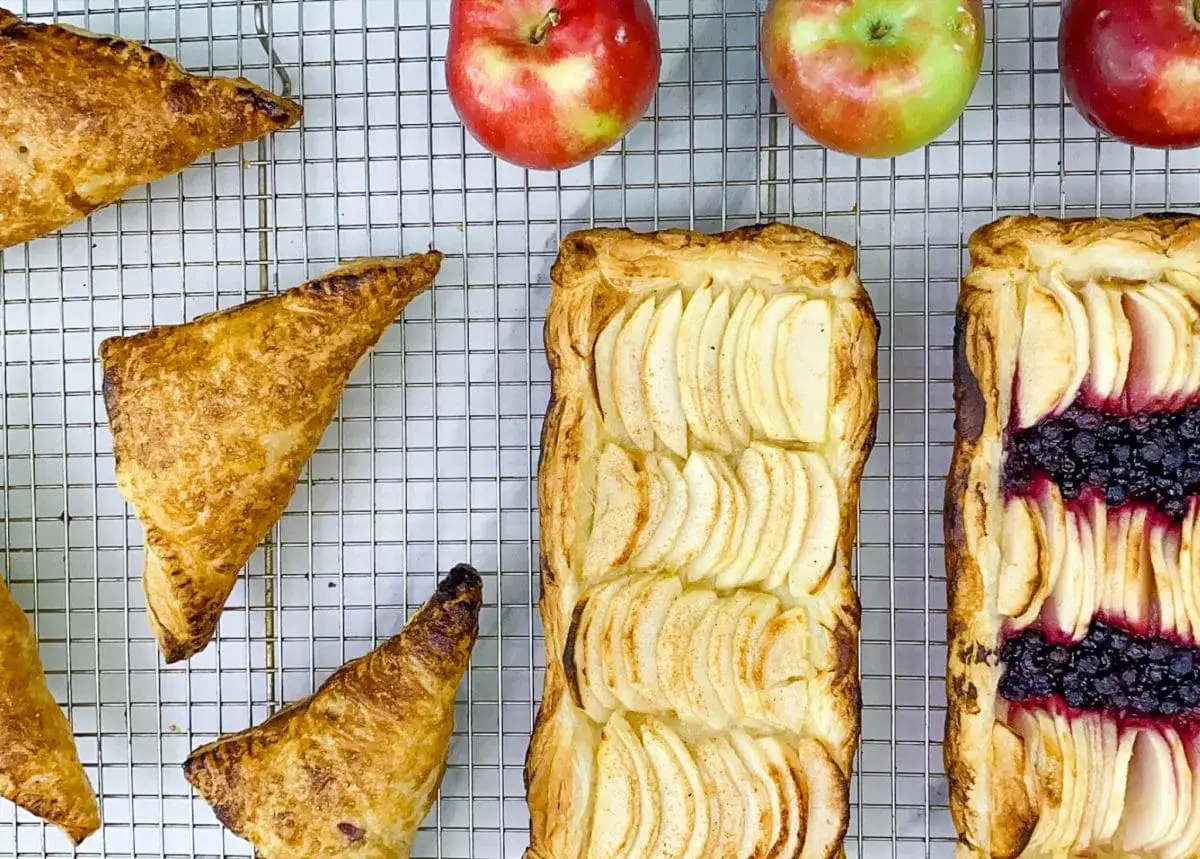 Délicieux chaussons aux pommes dorés et tartes aux pommes et myrtilles sur une grille. Des pommes fraîches sont disposées au-dessus.