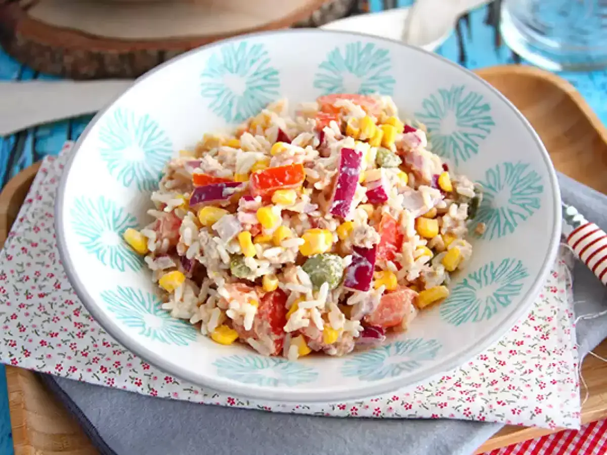 Une savoureuse salade de riz colorée avec du maïs, des poivrons rouges, des oignons rouges et du thon, servie dans un bol décoré.