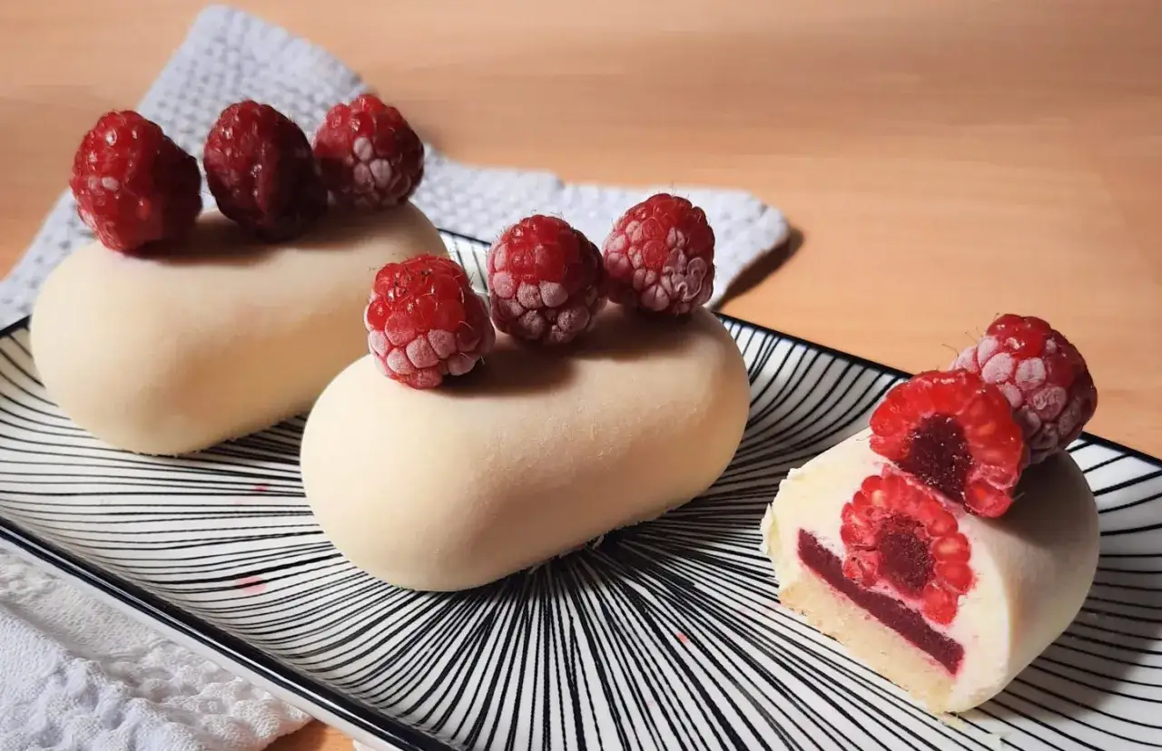 Gâteaux blancs ornés de framboises fraîches, révélant une cœur de purée de framboise intense.