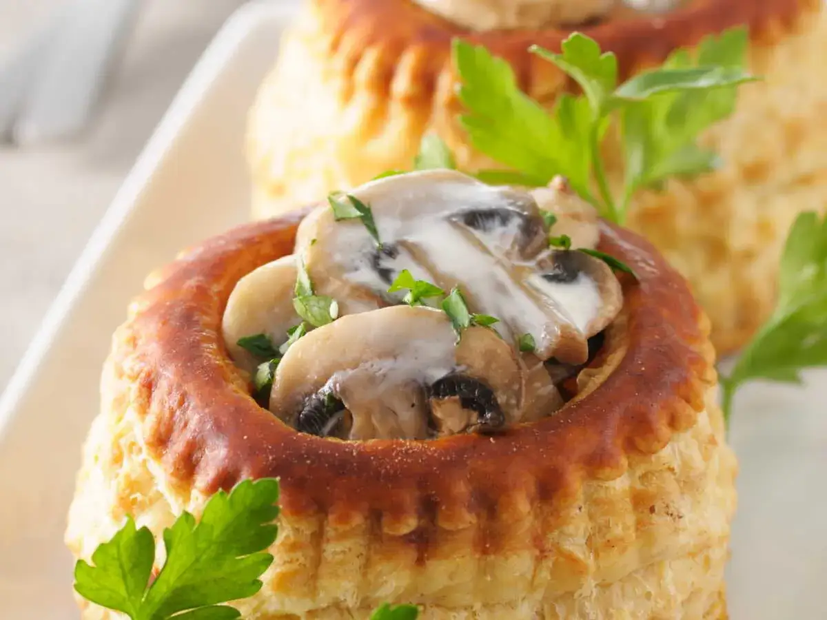 Une bouchée à la reine poulet, garnie de champignons crémeux et persil frais, dans une pâte feuilletée dorée.