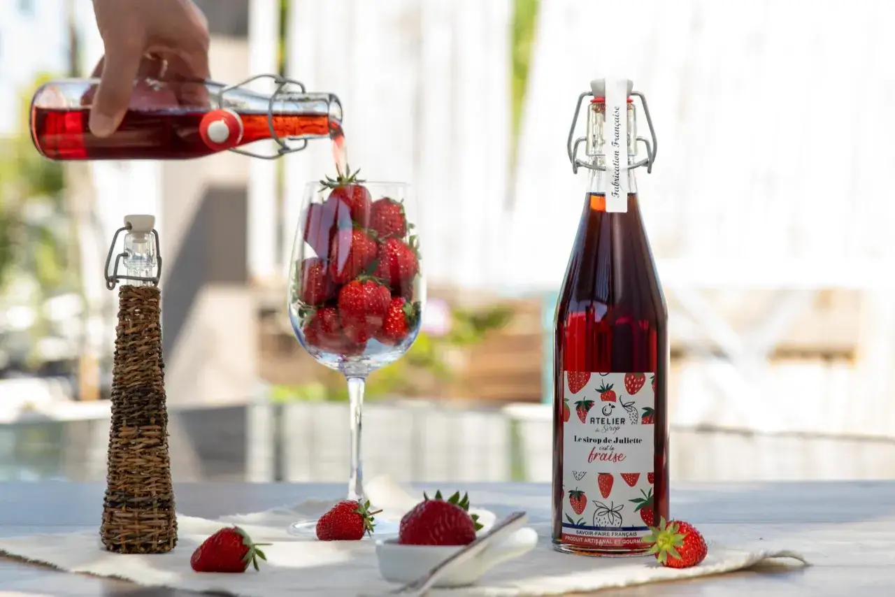 Le sirop de Juliette, un délice fruité à la fraise, est versé dans un verre rempli de fruits rouges. Une invitation à la gourmandise.