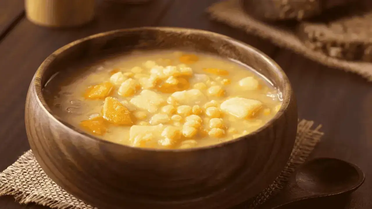 Un bol en bois rempli d'une réconfortante soupe de pois cassés, avec des morceaux de légumes et une cuillère en bois à côté.