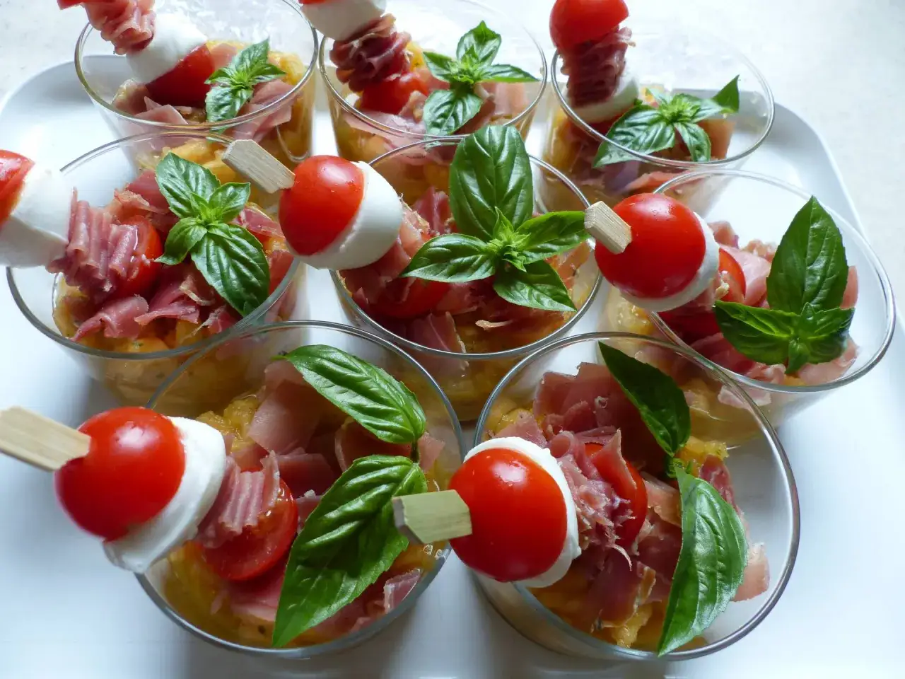 Verrines melon jambon cru : des brochettes tomate-mozzarella et basilic sur un lit de melon et jambon cru. Fraîcheur garantie !
