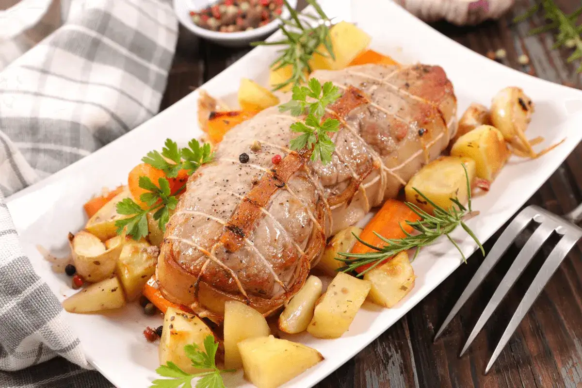 Roti de veau au four, savoureux et doré, servi avec des pommes de terre rôties, des carottes et des herbes fraîches.