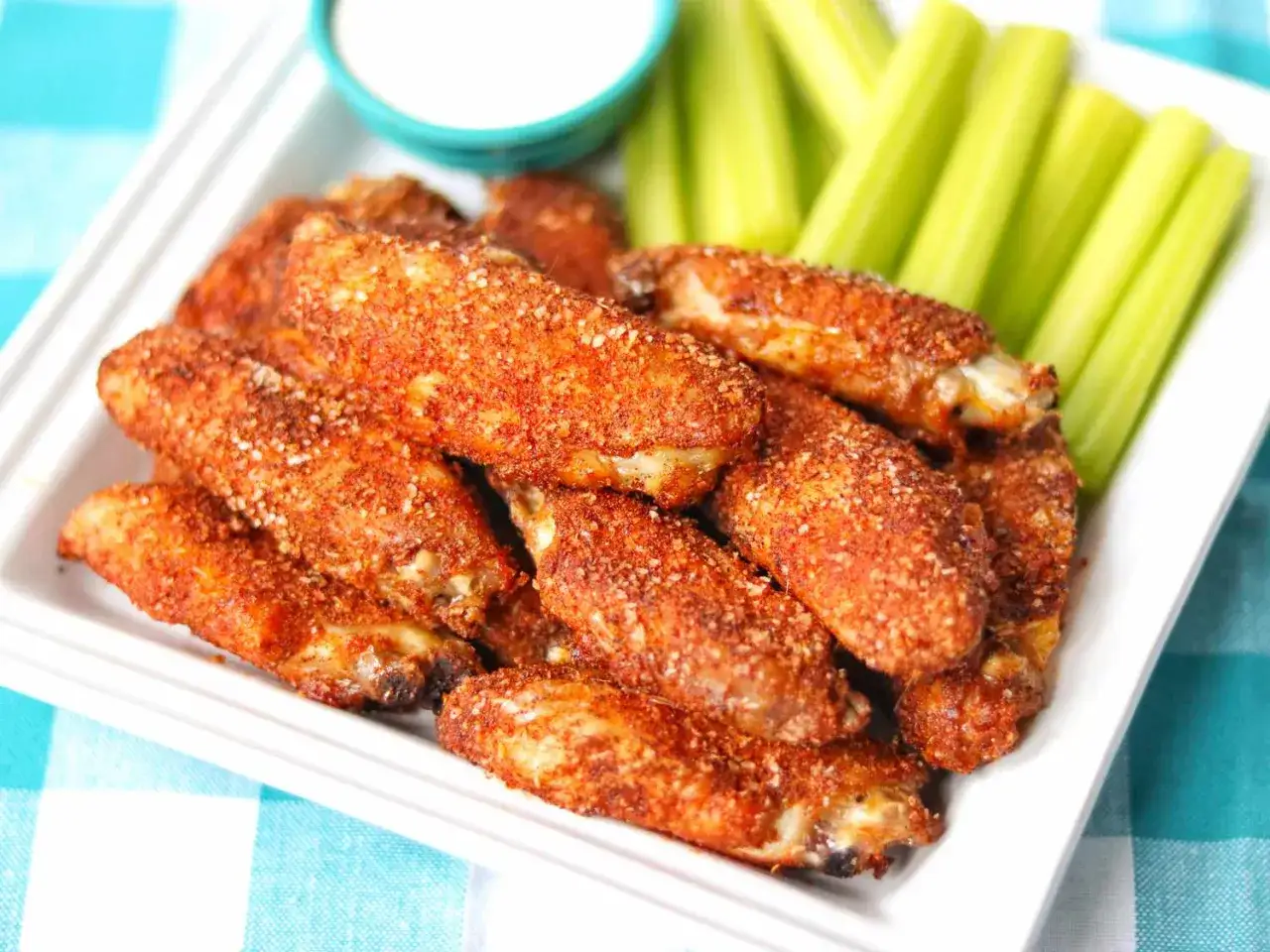 Assiette de chicken wings buffalo épicées, accompagnées de bâtonnets de céleri et d'une sauce blanche.