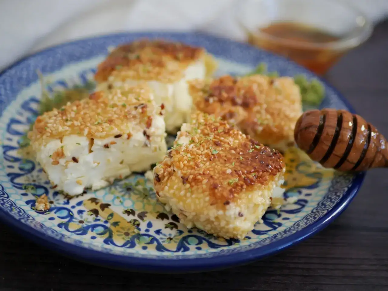 Feta grillée à la poêle, enrobée de sésame et servie sur une assiette décorée, avec un filet de miel.