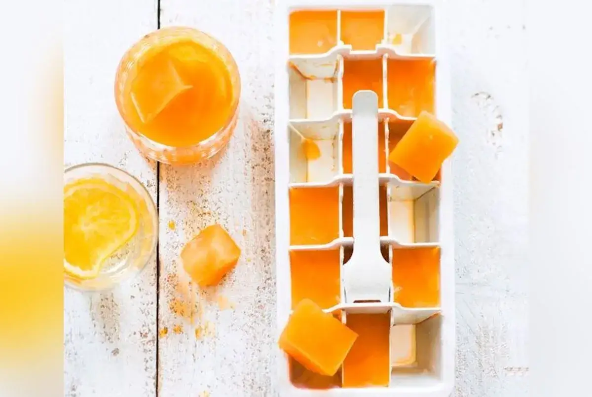 Composition Aperol Spritz : glaçons orange dans un bac, un verre avec une tranche d'orange et un autre verre rempli de glaçons et de liquide orange.