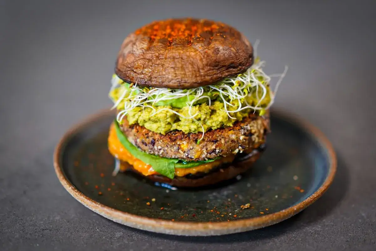 Burger végétarien gourmand : galette de haricots, avocat, pousses et champignon portobello grillé. Une recette savoureuse et saine.