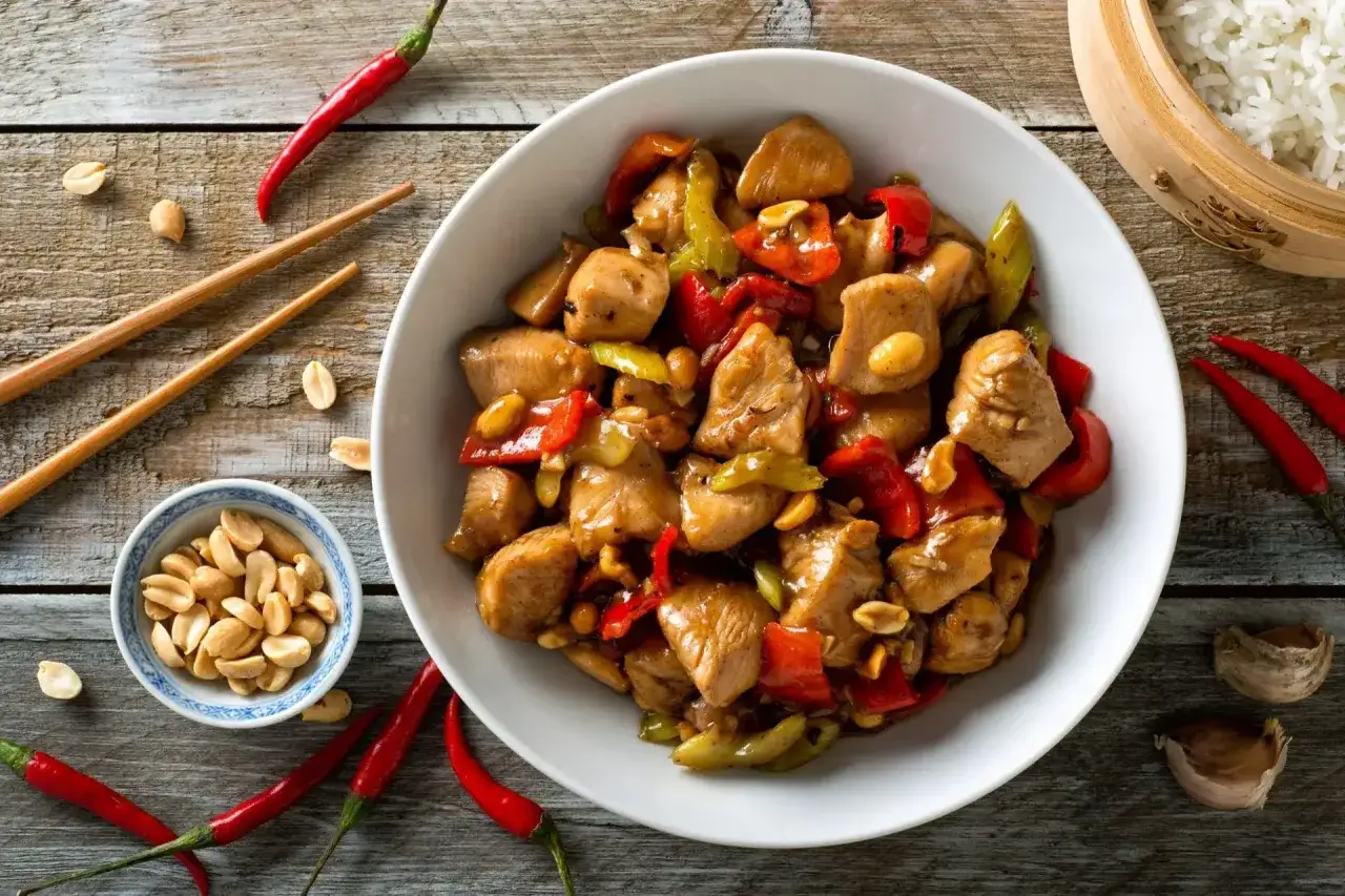 Un plat appétissant de poulet kung pao, garni de poivrons rouges et verts, d'arachides et de piments, prêt à être dégusté avec des baguettes.