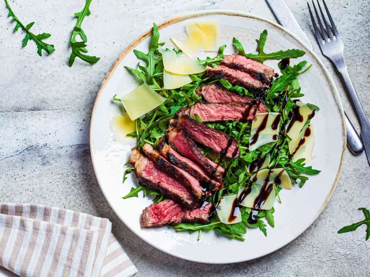 Une assiette de tagliata de boeuf, roquette, copeaux de parmesan et sauce balsamique.