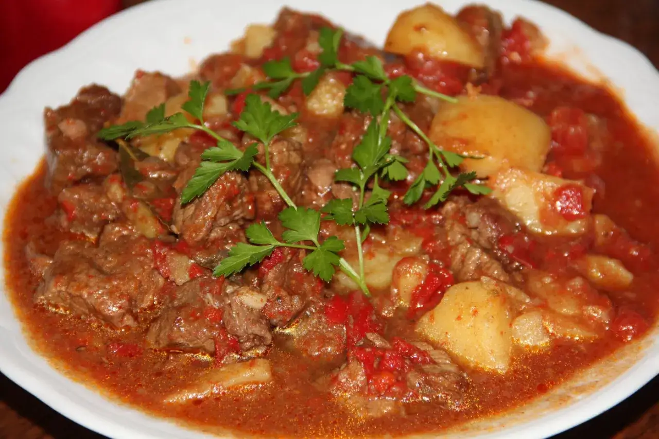 Un plat de recette goulash hongroise traditionnelle, avec des morceaux de bœuf tendres, des pommes de terre et une sauce riche, garni de persil frais.