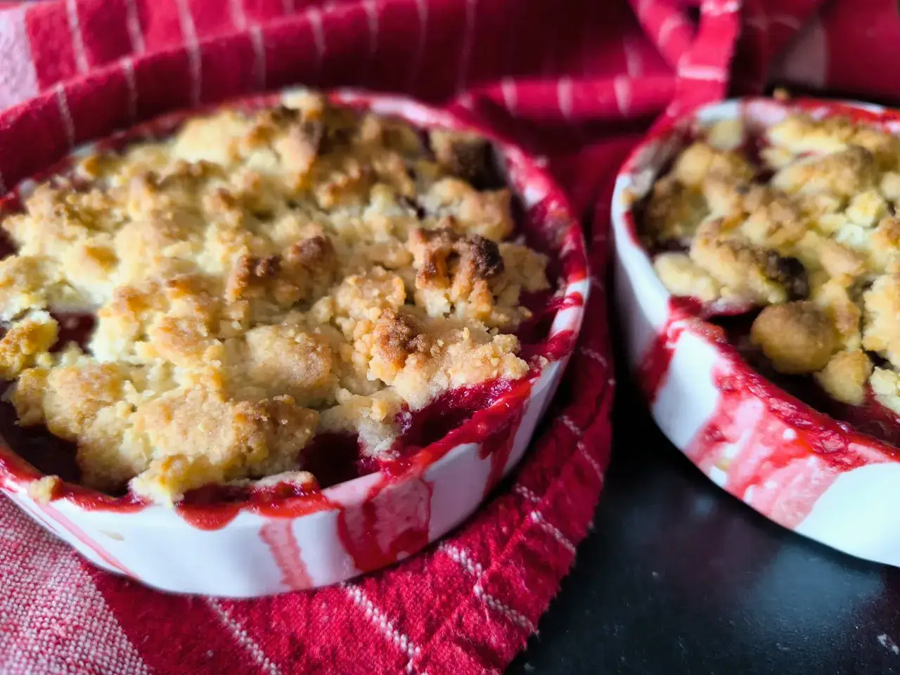 Deux ramequins de crumble fruits rouges, dorés et appétissants, sur un tissu rouge à rayures.