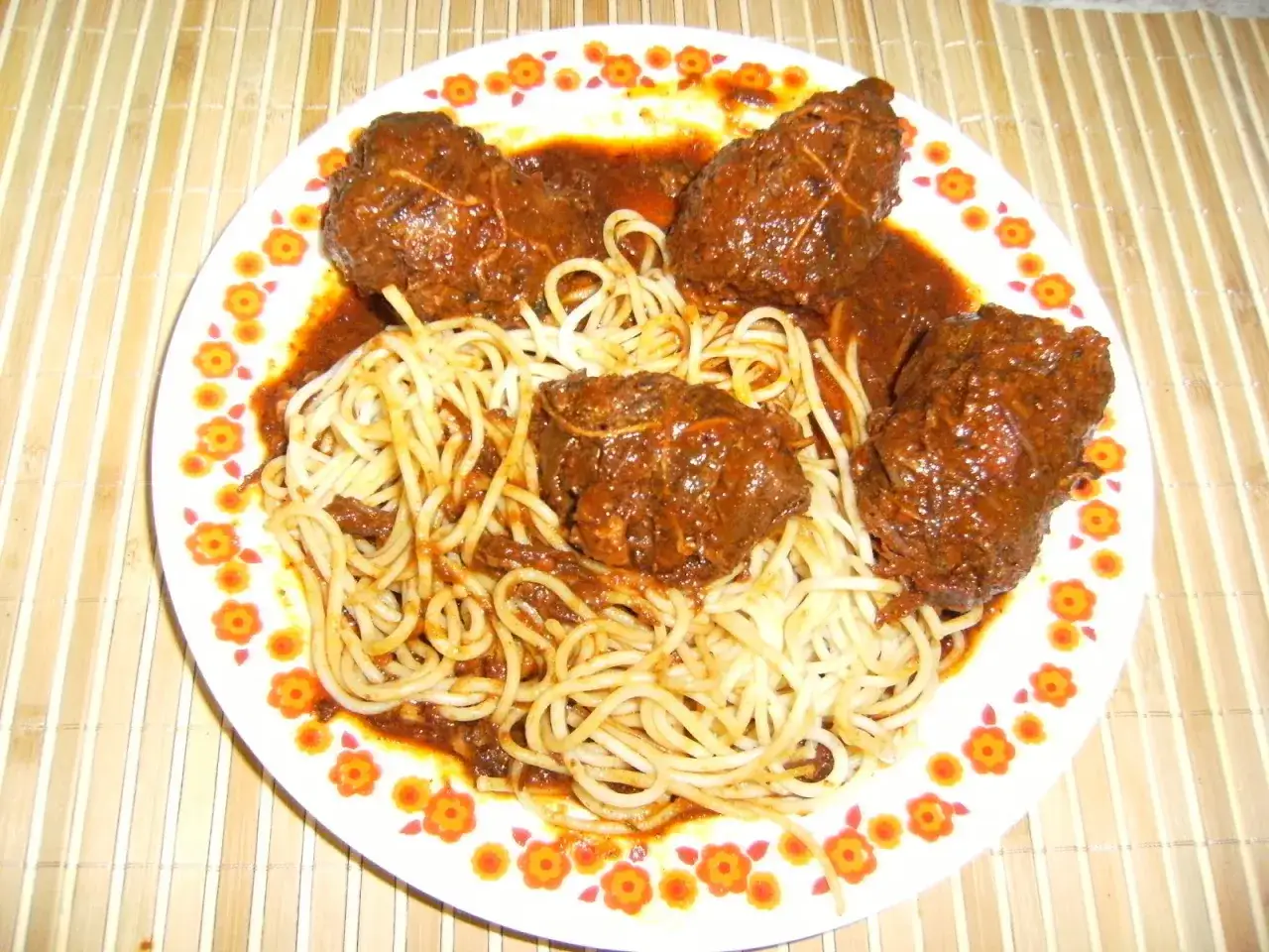 Assiette de spaghetti avec des ragoûts de bœuf en sauce, ressemblant à des alouettes sans tête, décorée de fleurs oranges.