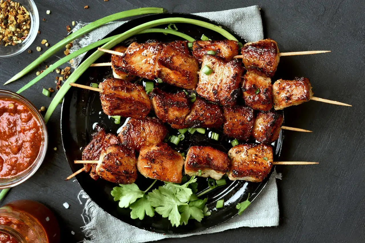 Brochettes de porc mariné grillées, garnies d'oignons verts et de coriandre, servies avec une sauce épicée.