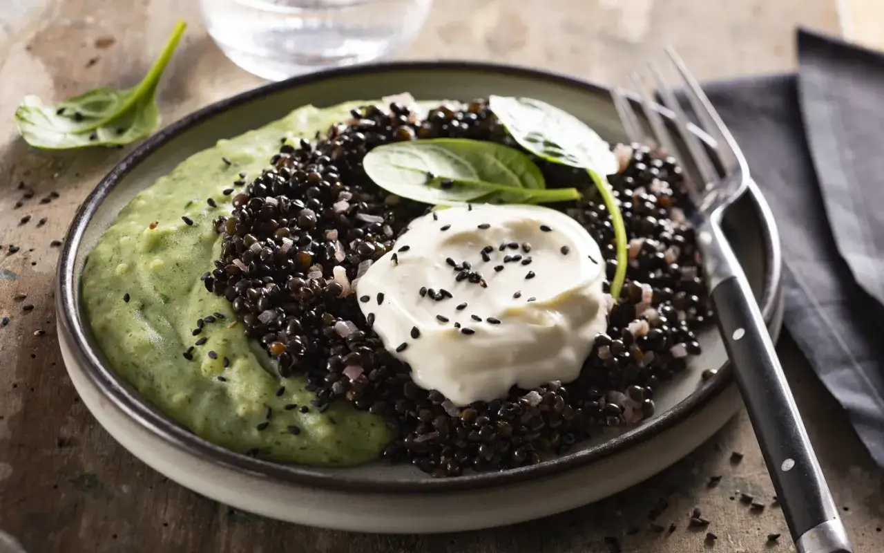 Assiette de lentilles beluga, purée verte et crème, garnie de graines de sésame noir. Un plat savoureux et visuellement attrayant.