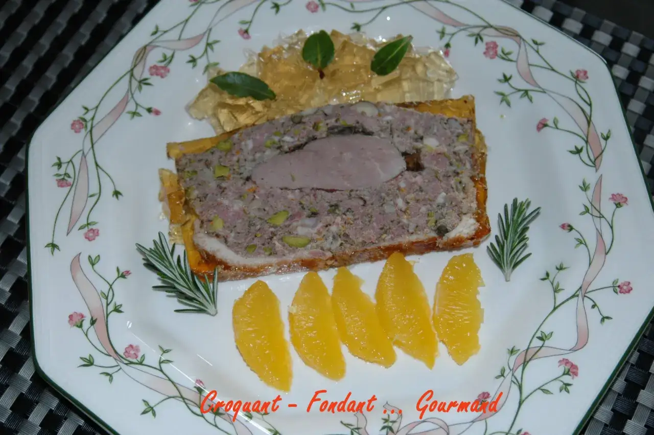 Tranche de terrine de canard, garnie de gelée et d'orange, sur une assiette décorée. Un délice croquant et fondant.