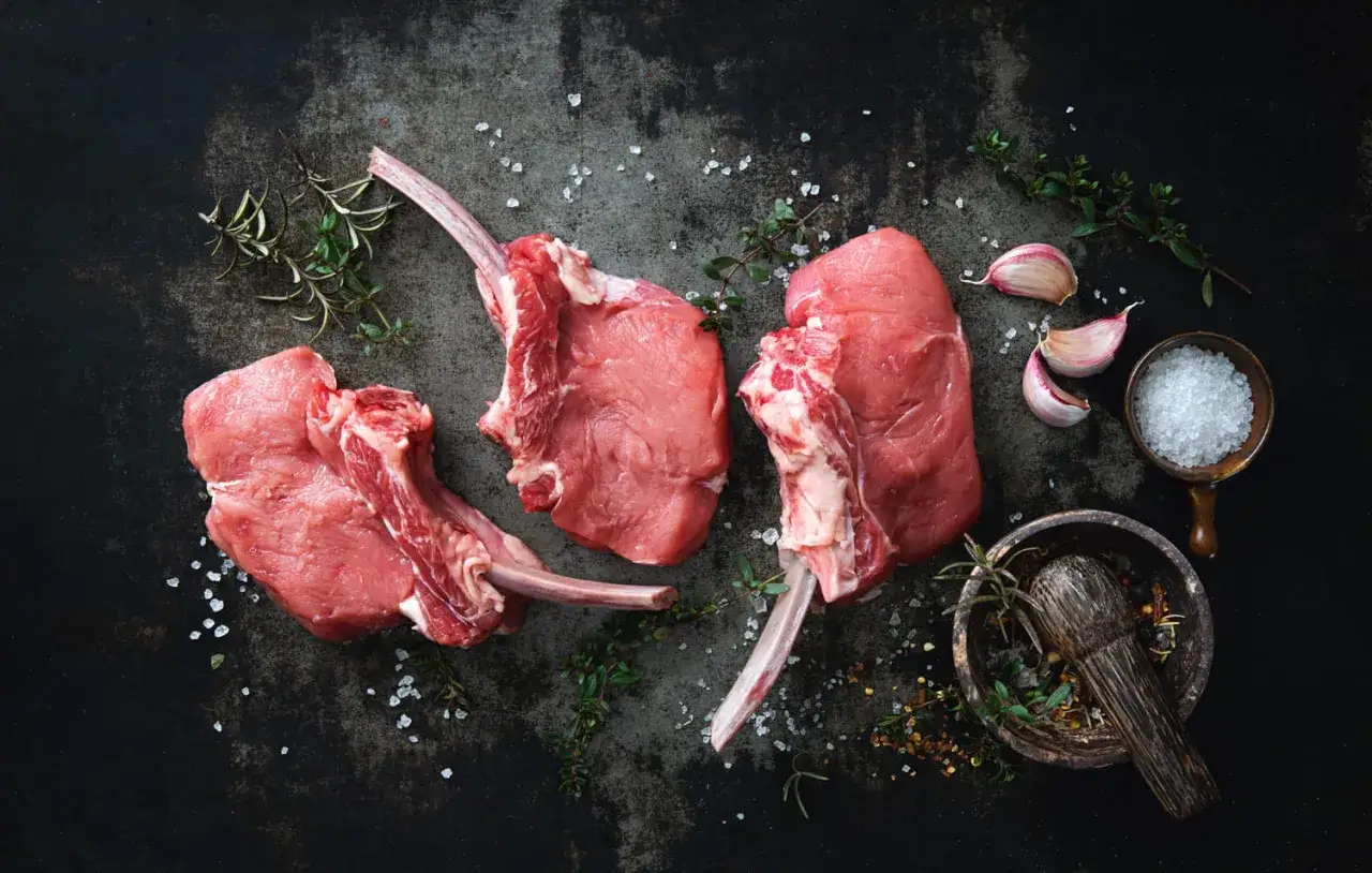 Trois t-bones de veau crus, prêts à être assaisonnés avec du gros sel, de l'ail et des herbes aromatiques.