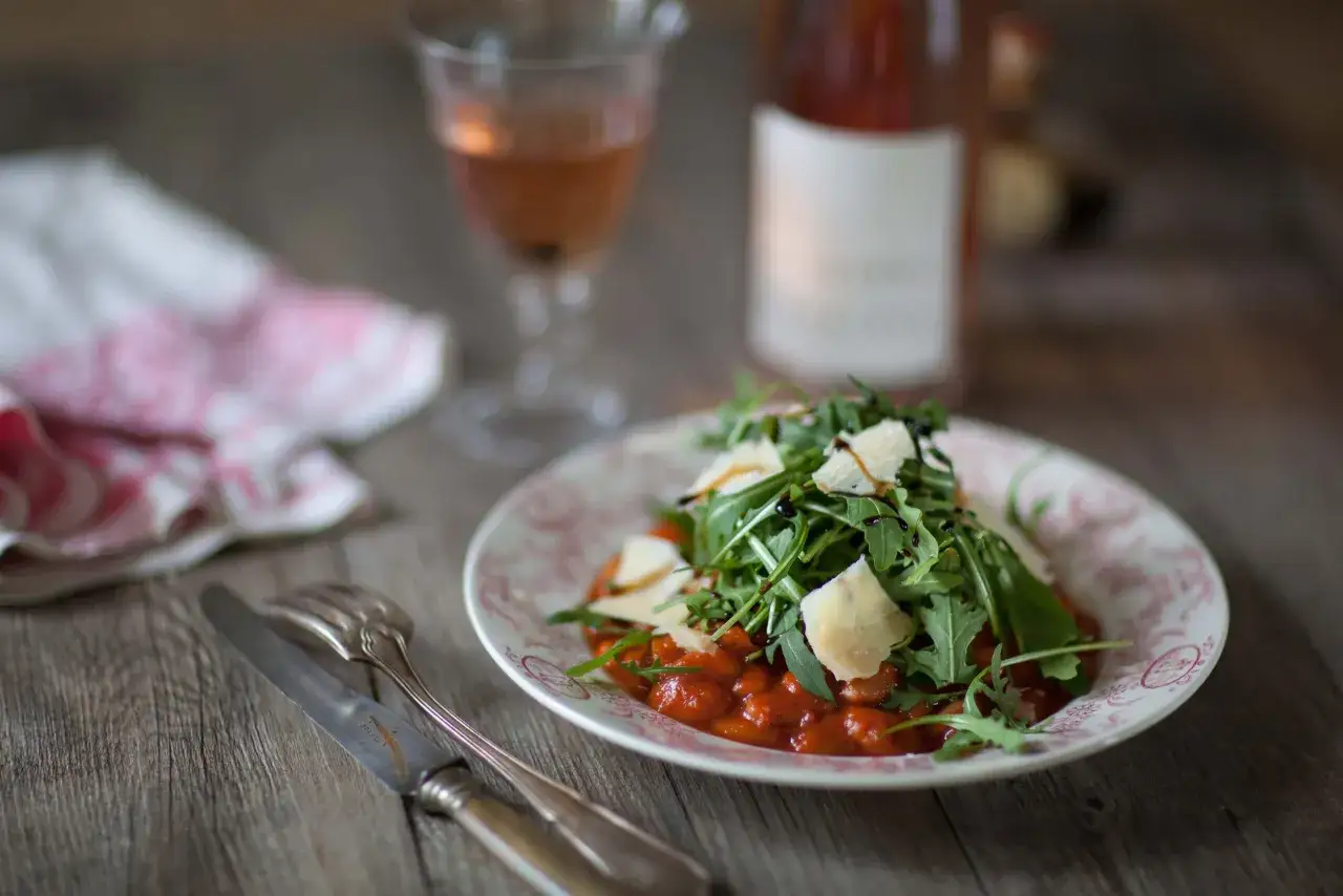 Une assiette de haricots blancs à la sauce tomate, garnie de roquette et de copeaux de parmesan. Parfait pour une recette baked beans facile et savoureuse.