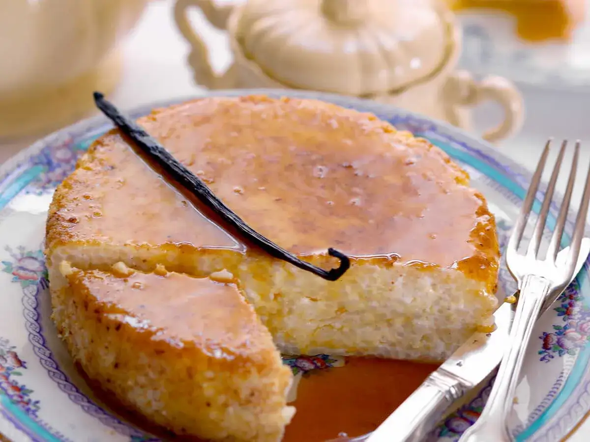 Un délicieux gâteau de riz crémeux, nappé d'un caramel doré et garni d'une gousse de vanille. Servi sur une assiette ornée, prêt à être dégusté.