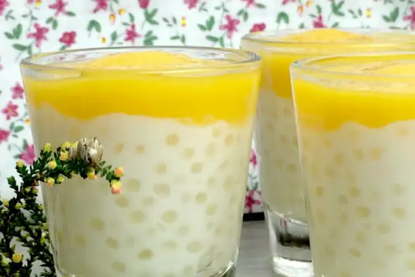 Trois verres de tapioca au lait de coco, surmontés d'une purée jaune, avec une petite branche de bruyère en premier plan.