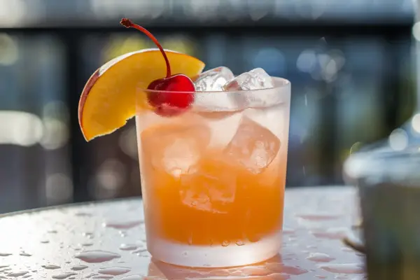 Cocktail rafraîchissant au jus d'abricot et alcool, garni d'une cerise et d'une tranche de pêche.